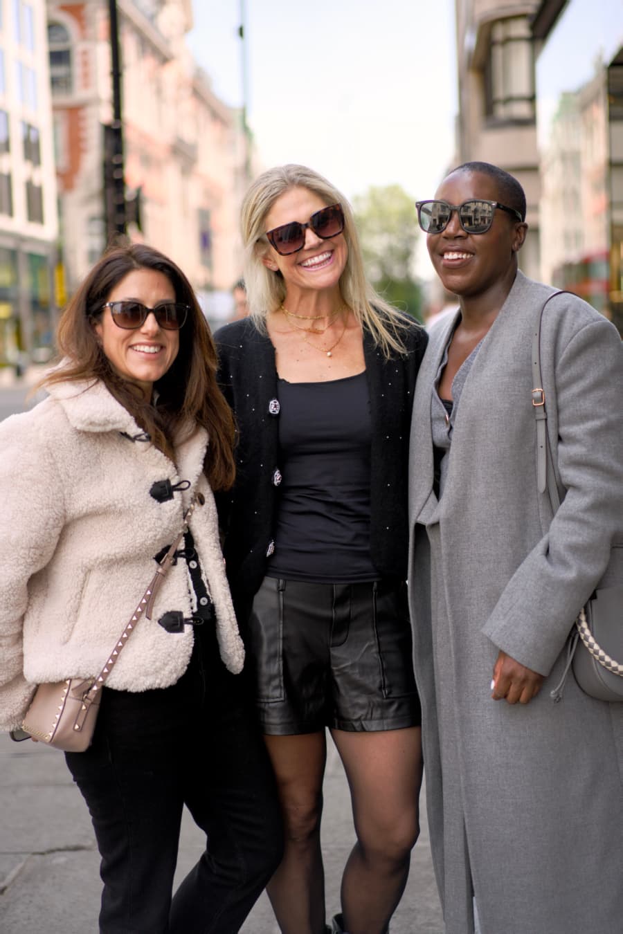 Three women laughing together arm in arm on a London street